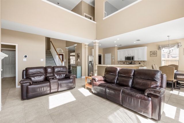 living area featuring stairs, light tile patterned flooring, a chandelier, and decorative columns