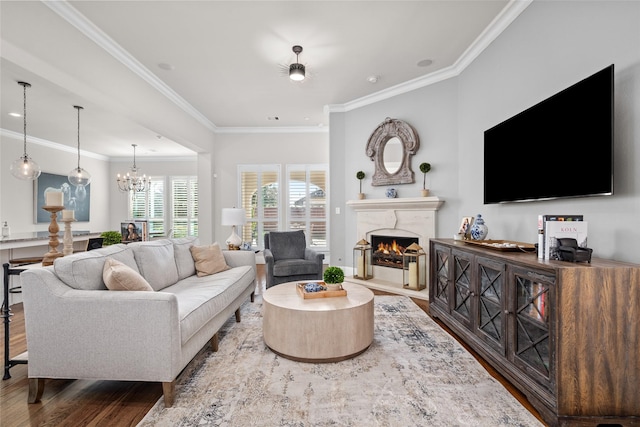 living area featuring a chandelier, ornamental molding, a fireplace, and wood finished floors