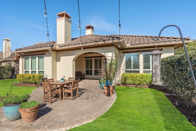 back of property featuring a patio, a tile roof, a lawn, stucco siding, and outdoor dining space