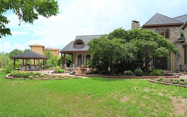 view of front facade featuring a front yard, stone siding, a chimney, and a gazebo