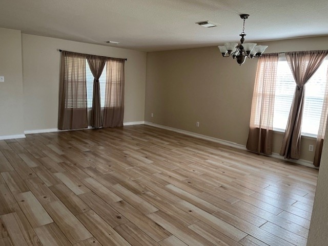 empty room featuring baseboards, visible vents, light wood finished floors, and an inviting chandelier