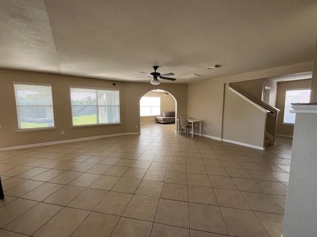 empty room featuring light tile patterned floors, baseboards, arched walkways, and a ceiling fan