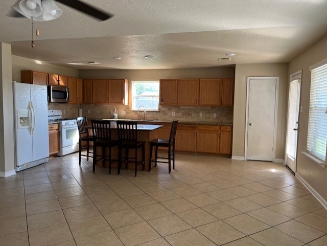 kitchen with backsplash, a kitchen island, a sink, white appliances, and a kitchen bar