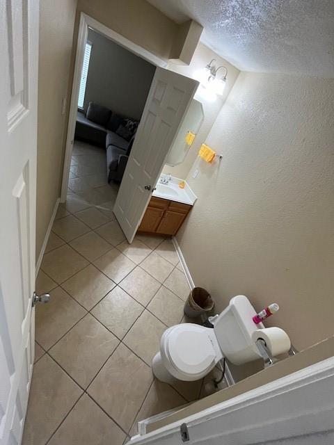 bathroom with baseboards, a textured wall, toilet, tile patterned flooring, and a textured ceiling