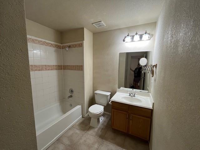 full bathroom with visible vents, a textured wall, toilet, tile patterned floors, and vanity