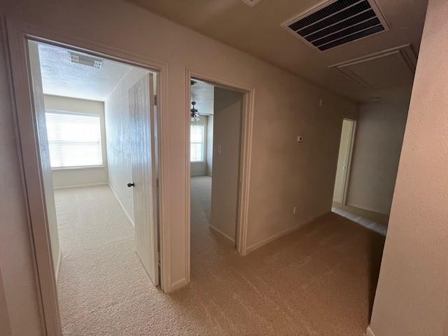 hallway featuring baseboards, carpet, visible vents, and attic access