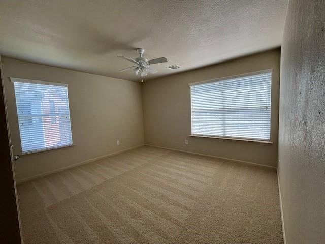 empty room featuring carpet, visible vents, ceiling fan, and a textured ceiling