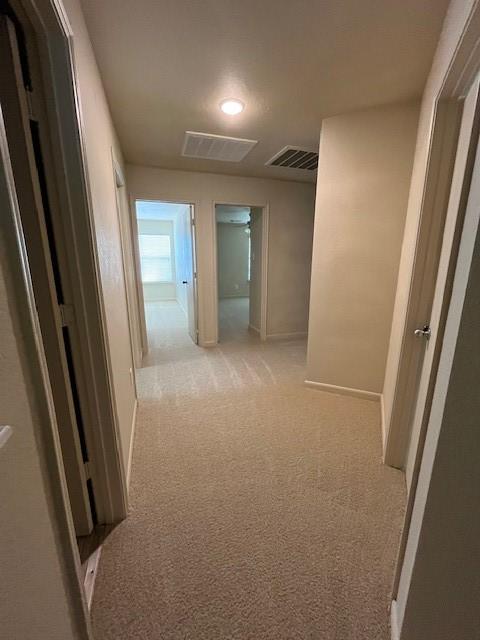 hallway featuring light carpet, visible vents, and baseboards