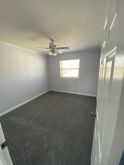 empty room with dark colored carpet, ceiling fan, and baseboards