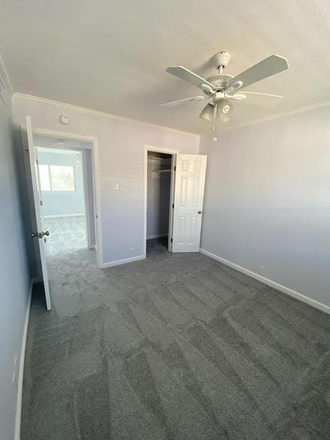 unfurnished bedroom with a ceiling fan, baseboards, ornamental molding, a closet, and dark colored carpet