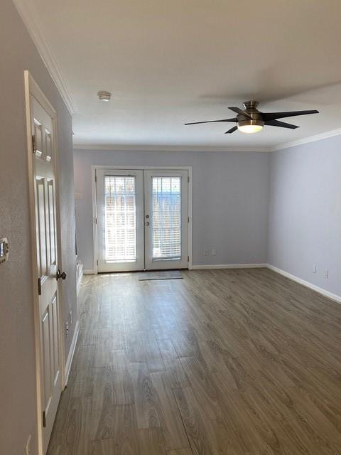 empty room featuring dark wood-style floors, french doors, baseboards, and crown molding