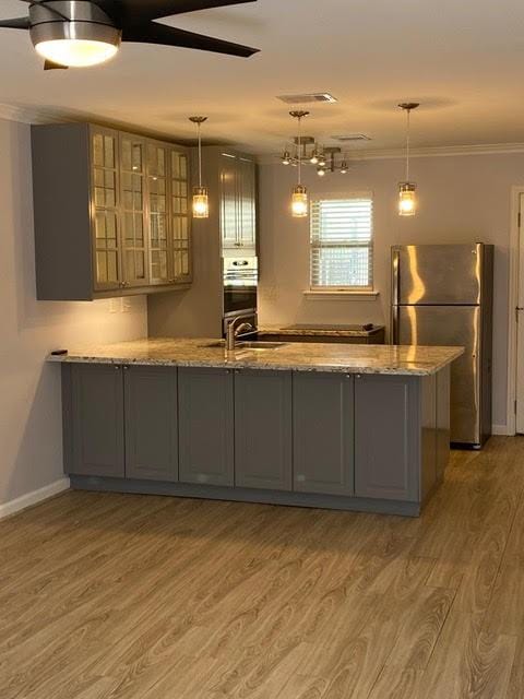 kitchen featuring light wood finished floors, gray cabinetry, freestanding refrigerator, light stone countertops, and a peninsula