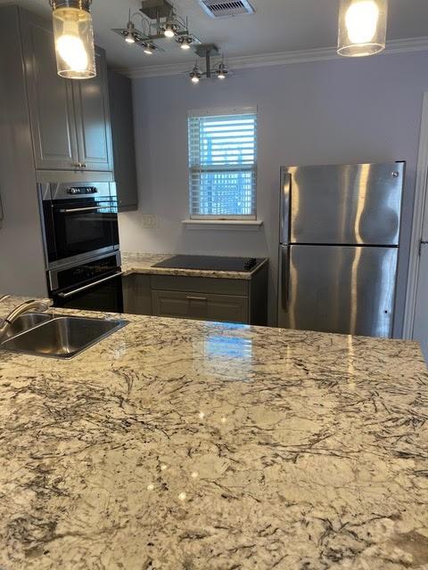 kitchen featuring light stone countertops, a sink, freestanding refrigerator, and crown molding