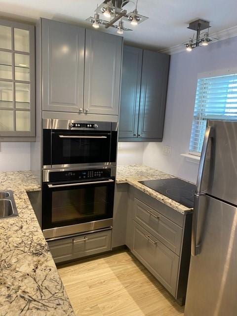 kitchen featuring appliances with stainless steel finishes, light stone countertops, light wood finished floors, glass insert cabinets, and an inviting chandelier