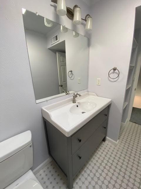 bathroom with toilet, vanity, visible vents, and baseboards