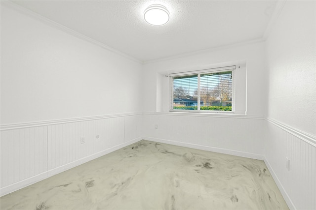 spare room featuring a textured ceiling, ornamental molding, concrete floors, and wainscoting