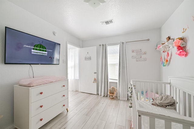 bedroom with light wood-type flooring, a nursery area, visible vents, and a textured ceiling