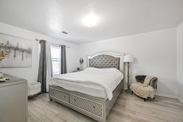 bedroom with a textured ceiling, light wood-type flooring, visible vents, and baseboards