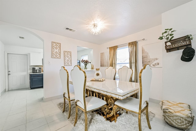 dining room featuring arched walkways, visible vents, baseboards, and light tile patterned floors