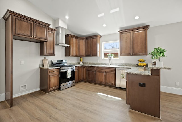 kitchen with stainless steel appliances, wall chimney exhaust hood, a peninsula, and light wood-style floors