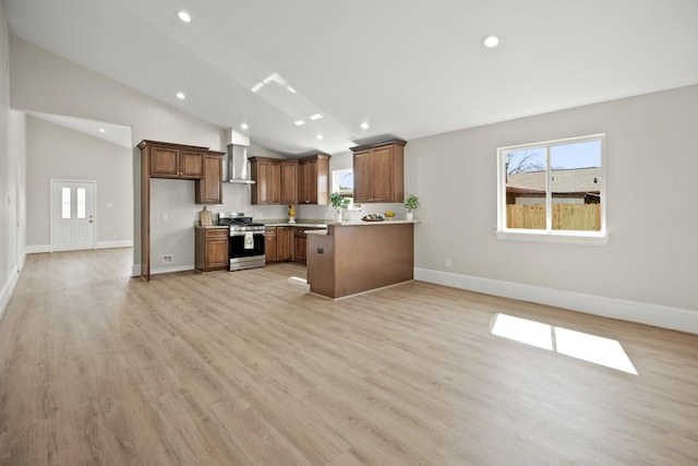 kitchen featuring stainless steel range with gas cooktop, lofted ceiling, light countertops, light wood-style floors, and wall chimney range hood