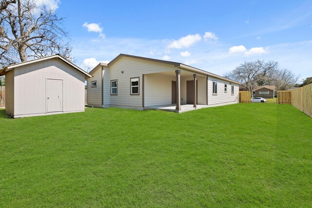rear view of house with an outbuilding, a yard, a storage shed, a patio area, and fence