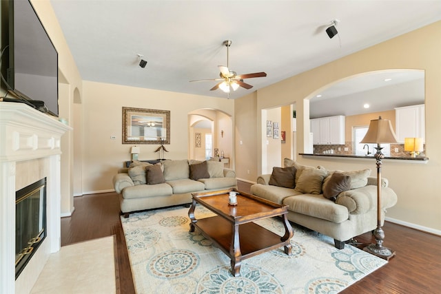 living area featuring arched walkways, recessed lighting, a glass covered fireplace, wood finished floors, and baseboards