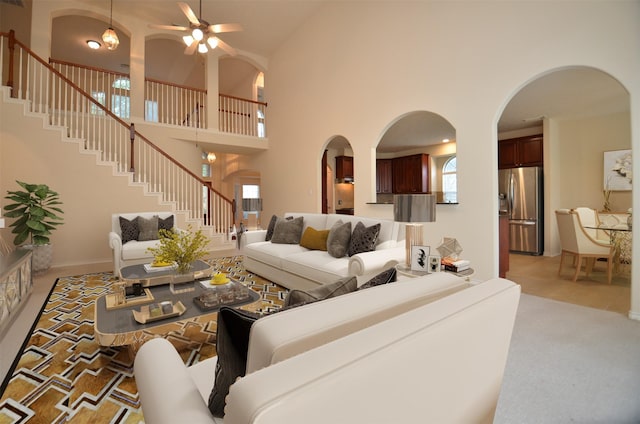 living area with stairway, a ceiling fan, baseboards, a high ceiling, and light colored carpet