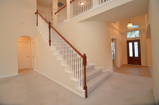 entryway featuring arched walkways, baseboards, carpet, and a towering ceiling