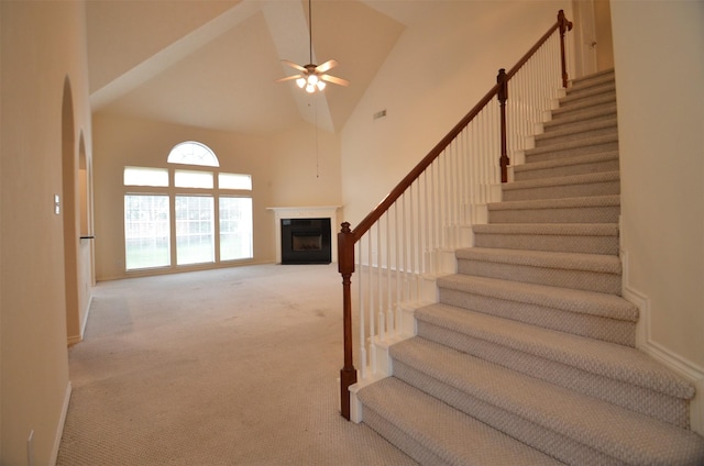 stairs featuring carpet, visible vents, high vaulted ceiling, a fireplace, and ceiling fan