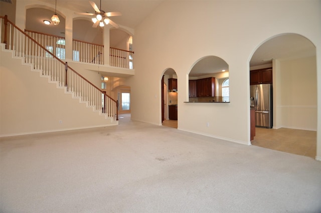 unfurnished living room with baseboards, stairway, light colored carpet, a high ceiling, and a ceiling fan