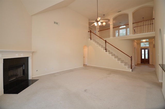 unfurnished living room with carpet, ceiling fan, a fireplace with flush hearth, arched walkways, and high vaulted ceiling