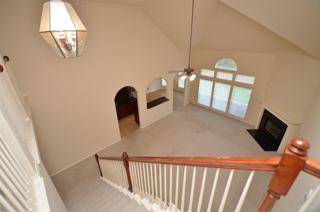 staircase with a ceiling fan, baseboards, high vaulted ceiling, a fireplace with flush hearth, and carpet flooring