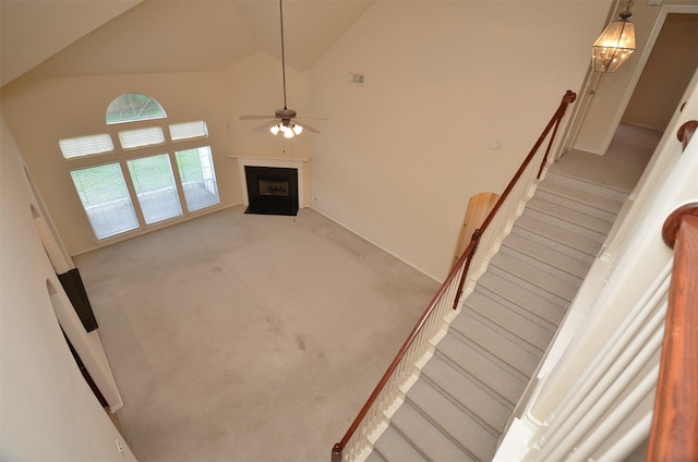 stairway with visible vents, high vaulted ceiling, a fireplace with flush hearth, ceiling fan, and carpet flooring