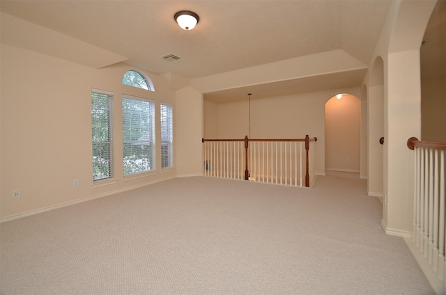 empty room featuring light carpet, baseboards, visible vents, and arched walkways