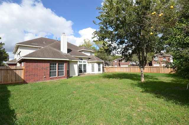 rear view of property with brick siding, a fenced backyard, a chimney, and a yard