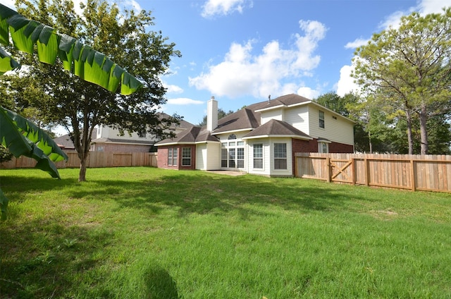 rear view of property with brick siding, a fenced backyard, a chimney, and a yard