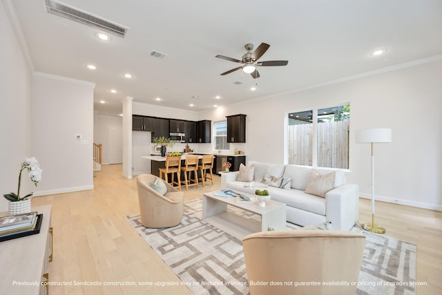 living area featuring baseboards, visible vents, crown molding, and light wood finished floors