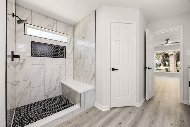 bathroom with a tile shower, baseboards, and wood finished floors