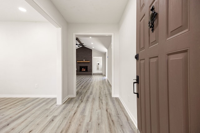 corridor featuring lofted ceiling, light wood-style flooring, and baseboards