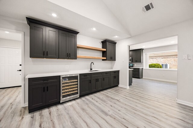 bar with vaulted ceiling, visible vents, a sink, beverage cooler, and light wood finished floors