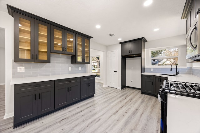 kitchen with stainless steel microwave, backsplash, black gas range oven, light wood-style floors, and a sink