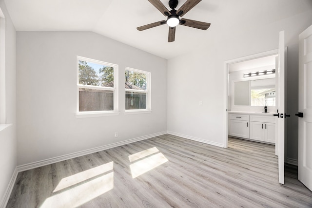 unfurnished bedroom featuring light wood finished floors, baseboards, vaulted ceiling, and ensuite bathroom