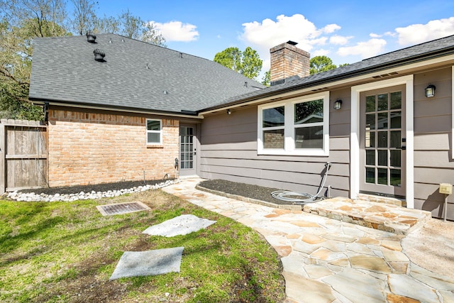 rear view of property featuring brick siding, roof with shingles, a chimney, a patio area, and fence