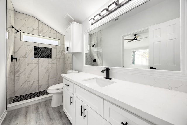 bathroom featuring toilet, lofted ceiling, wood finished floors, a tile shower, and vanity