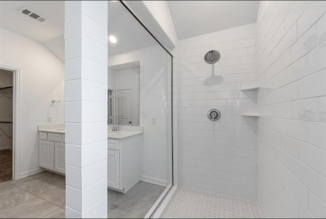 bathroom featuring a walk in closet, visible vents, vanity, and tiled shower