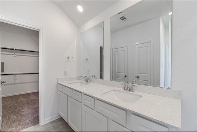 bathroom featuring a walk in closet, visible vents, a sink, and double vanity