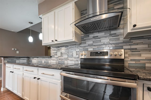 kitchen with wall chimney range hood, stainless steel electric range oven, white cabinetry, and wood finished floors