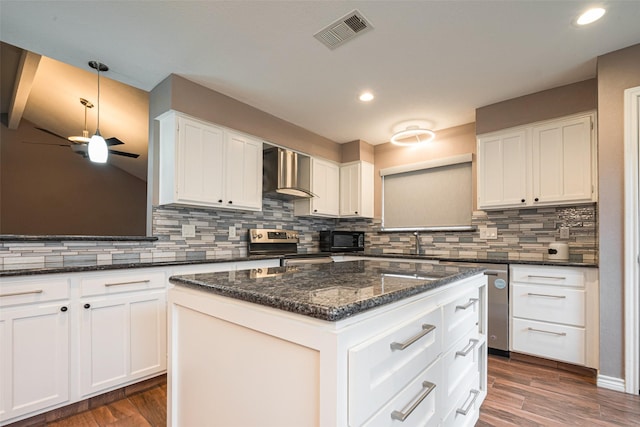 kitchen with visible vents, white cabinets, stainless steel appliances, wall chimney range hood, and a sink