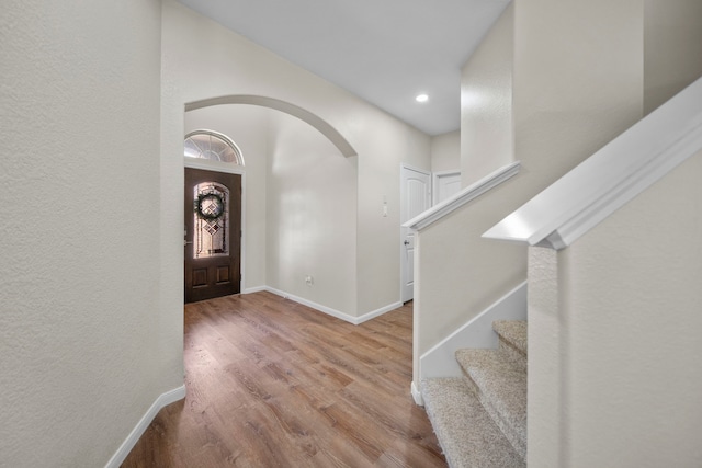 foyer entrance with baseboards, arched walkways, wood finished floors, stairs, and recessed lighting